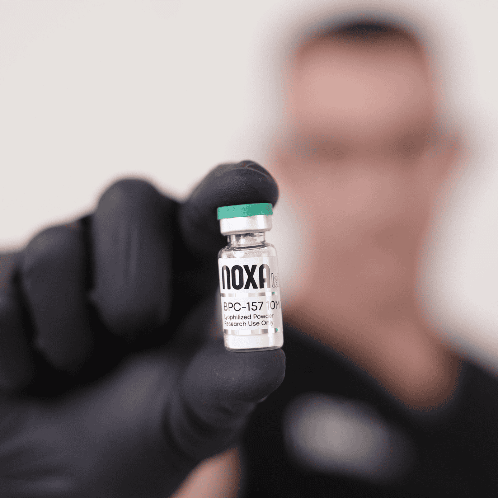 BPC-157 Close-up of Noxa Labs vaccine vial held by gloved hand, blurred background.